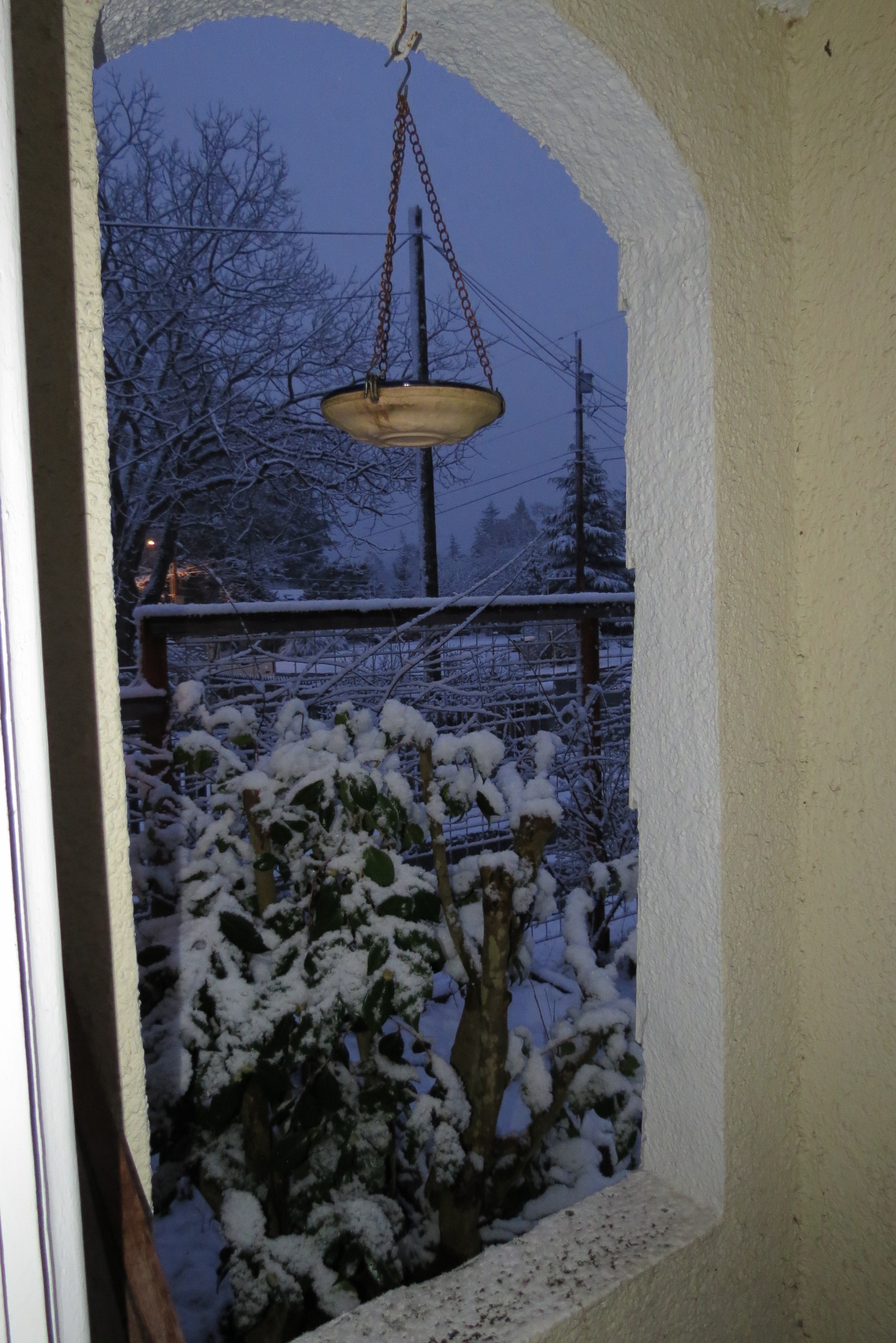 archway in the evening, with a hanging birdbath and snow on a yard, all blue light